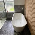 London builders and electricians renovating a modern bathroom with freestanding bathtub, tiled floor and walk‑in shower.