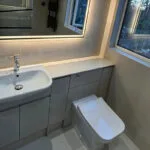 London builders and electricians renovating a compact bathroom with modern fixtures, vanity unit and backlit mirror.